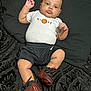 baby, infant, child, person, face, clothing, onesie, shorts, sneakers, nike, basketball_logo, black_blanket, patterned_blanket, lying_down, indoor, cute, chubby_cheeks, wide_eyes, footwear, sportswear
