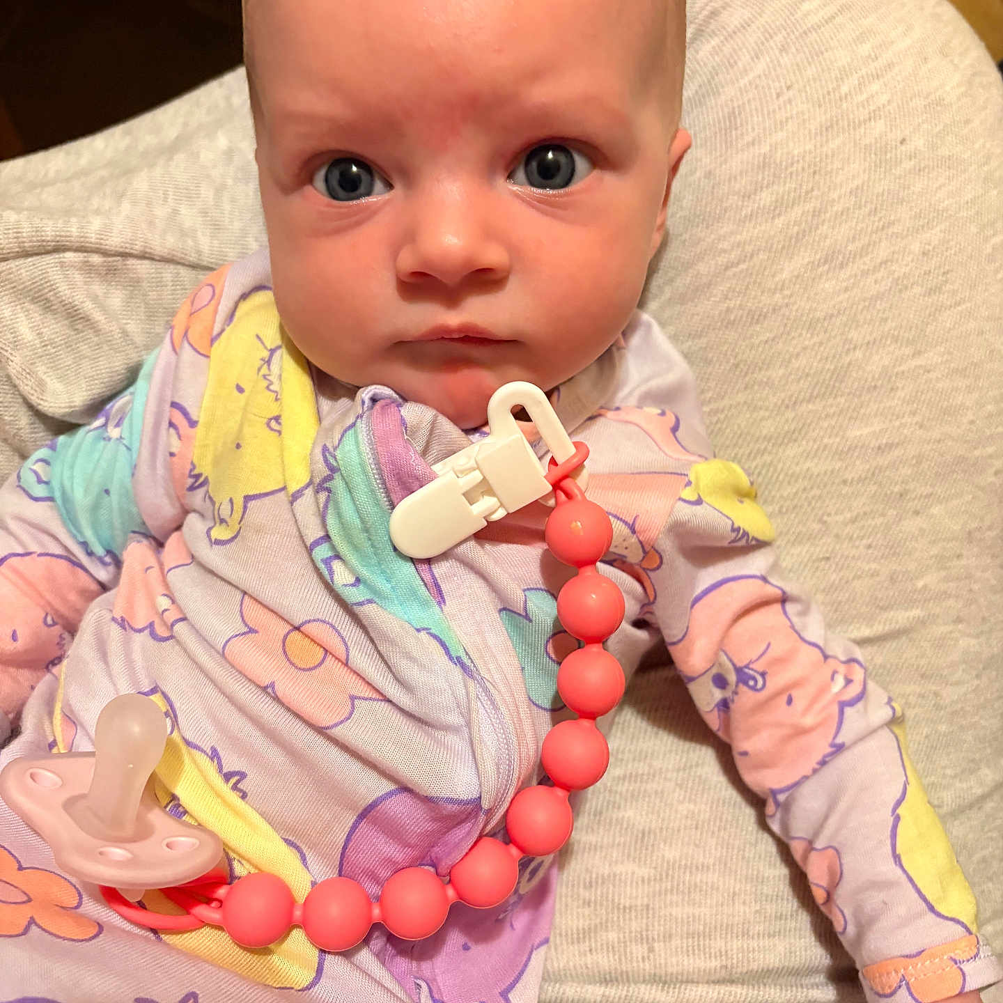 Layla joined the competition — help win amazing prizes! baby, infant, pacifier, pajamas, clothing, face, person, child, indoors, expression, cute, skin, hand, head, blue_eyes, fabric, comfort, holding, clip, beads