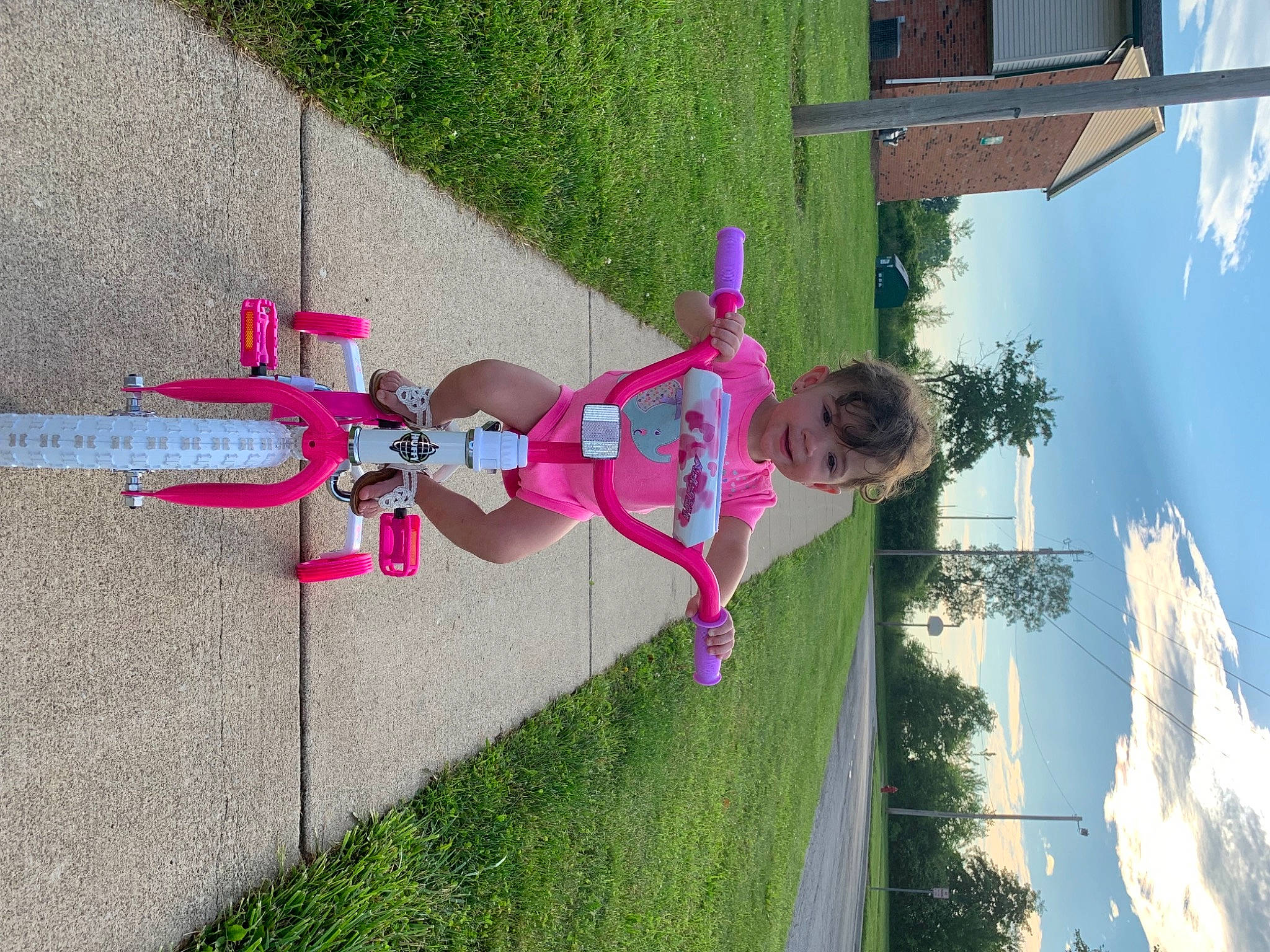 Paizley is registered to the contest to win money with this photo: bicycle_handlebar, cloud, concrete, fun, grass, house, joy, leisure, line, magenta, person, plant, pole, recreation, shadow, sidewalk, sky, tire, toddler, tree