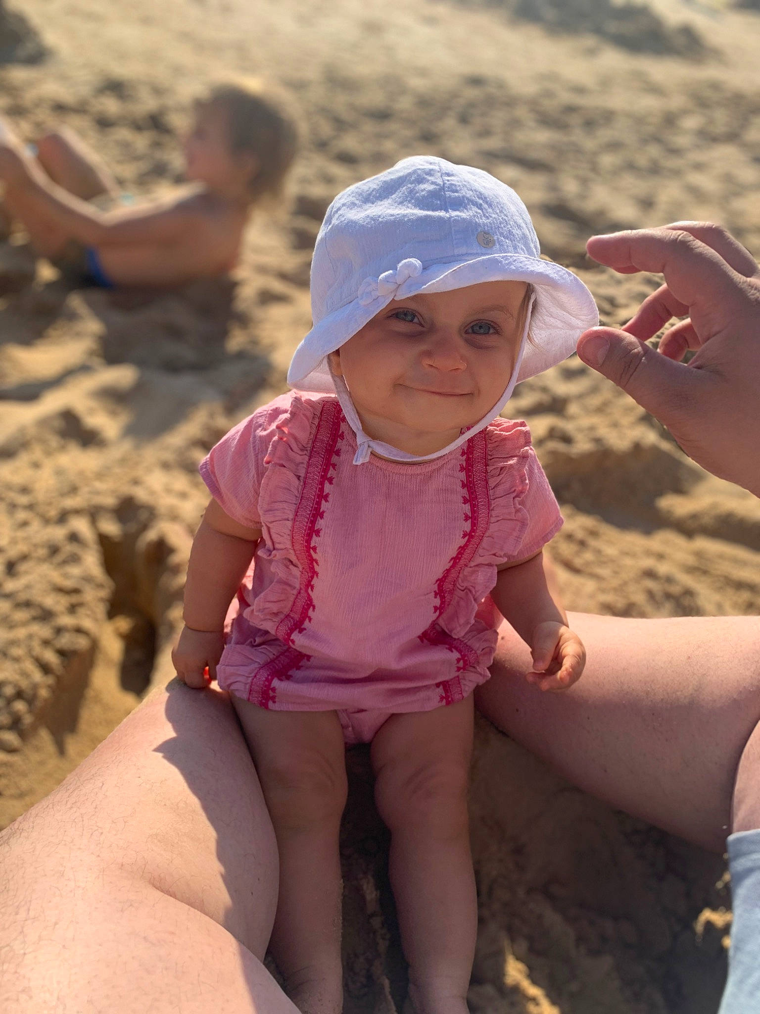 Anaël participe au concours pour gagner de l'argent avec cette photo : baseball_cap, beach, blurred, cap, child, fun, happy, hat, headwear, human_leg, joy, leg, leisure, mammal, people_on_beach, person, personal_protective_equipment, recreation, sand, sitting