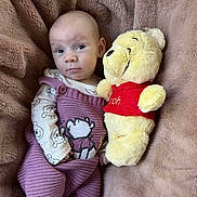 Ruth joined the competition — help win amazing prizes! baby, infant, plush_toy, winnie_the_pooh, blanket, knitted_clothing, purple_outfit, cute, soft_toy, bedroom, cozy, child, smiling, portrait, indoor, baby_clothes, stuffed_animal, lying_down, comfortable, toddler