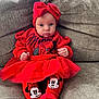 baby, child, red_clothing, headband, bow, minnie_mouse, tights, sitting, sofa, couch, indoors, cute, infant, portrait, person, toddler, smiling, cozy, furniture, fashion