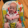 baby, infant, smile, baby_seat, colorful, patterned, wooden_floor, clothing, happy, child, indoor, seat_belt, cute, portrait, person, young_child, sitting, hands, face, caucasian