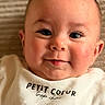 Noah a rejoint le concours — aidez-le/la à gagner de superbes lots ! baby, infant, face, eyes, cheeks, smile, white_shirt, text_on_clothing, closeup, portrait, skin, head, person, young_child, cute, soft_light, indoors, expression, happy, lying_down