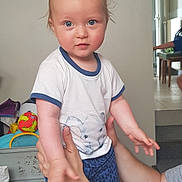 Dean a rejoint le concours — aidez-le/la à gagner de superbes lots ! child, baby, toddler, face, blue_eyes, blond_hair, tshirt, shorts, hands, arms, holding, smile, indoor, living_room, toy, ball, parent, furniture, bed, portrait