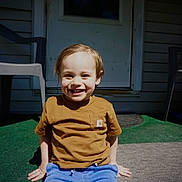 Colt joined the competition — help win amazing prizes! child, toddler, smiling, outdoor, door, plastic_chair, green_carpet, sunlight, casual_clothing, happy, sitting, brown_shirt, blue_pants, front_yard, shadow, person, daylight, home, porch, young_child