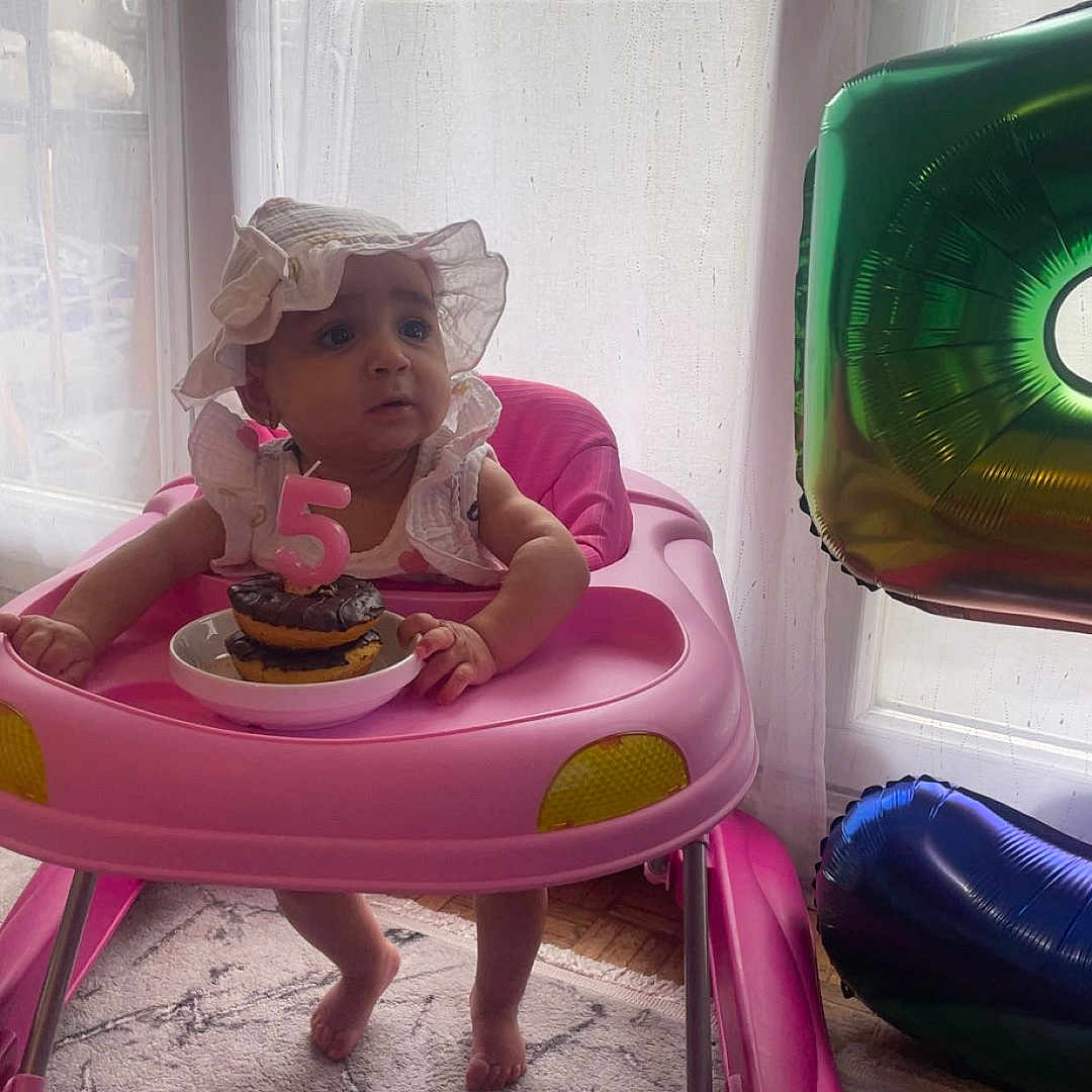 Emanuella a rejoint le concours — aidez-le/la à gagner de superbes lots ! baby, balloon, birthday, candle, carpet, celebration, child, curtain, cute, donut, floor, foot, hat, indoor, infant, person, pink, plate, walker, window