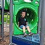 child, playground, slide, green, tunnel, outdoor, park, grass, clothing, shorts, shoes, person, leisure, daylight, fun, play, casual, kid, recreation, equipment