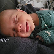 Owen is registered to the contest to win money with this photo: baby, smile, sleeping, green_clothing, closeup, peaceful, infant, resting, soft_surface, hand, face, cozy, cute, child, portrait, apparel, comfort, young, skin, relaxation