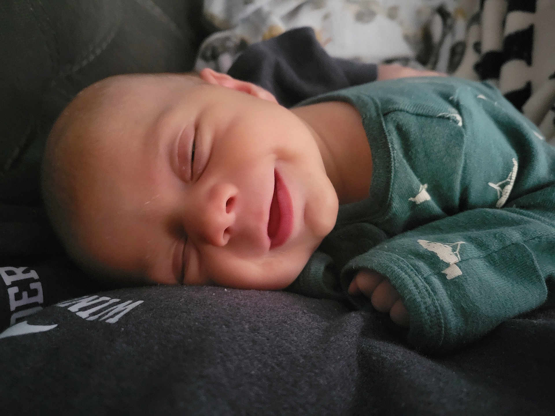 Owen is registered to the contest to win money with this photo: baby, smile, sleeping, green_clothing, closeup, peaceful, infant, resting, soft_surface, hand, face, cozy, cute, child, portrait, apparel, comfort, young, skin, relaxation
