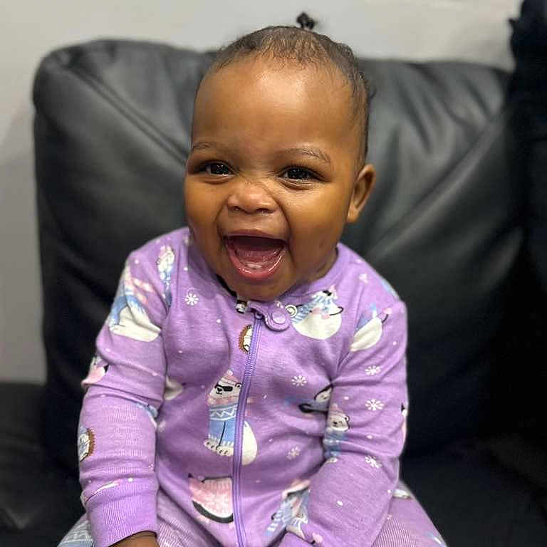 Khalissa joined the competition — help win amazing prizes! baby, child, smiling, laughing, purple_onesie, animal_prints, toy, red_toy, sitting, black_leather_couch, indoor, happy, cute, infant, young_child, face, expression, clothing, joyful, portrait