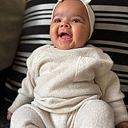 Alaiyah is registered to the contest to win money with this photo: baby, child, smiling, headband, bow, knitwear, sitting, cushion, striped, clothing, happy, infant, portrait, indoor, cute, fashion, cozy, person, face, expression