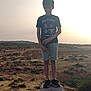 Adam participe au concours pour gagner de l'argent avec cette photo : child, boy, standing, concrete_pillar, tshirt, shorts, shoes, outdoor, sunset, field, grass, hill, nature, landscape, person, casual_clothing, daylight, sky, scenery, young