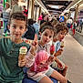 child, children, ice_cream, cone, bench, shopping_mall, indoor, people, casual_clothing, curly_hair, smiling, playful, food, dessert, retail, storefront, public_space, family, leisure, happy