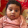 baby, infant, child, pink_clothing, sitting, face, eyes, hair, indoors, couch, patterned_background, red, gold, curious, portrait, young_child, closeup, soft_fabric, comfortable, casual
