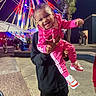 toddler, child, person, smile, pink_tracksuit, sneakers, beads, night, carnival, ferris_wheel, lights, amusement_park, holding, joyful, outdoor, tree, adult, people, fun, celebration