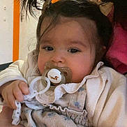 Ayla participe au concours pour gagner de l'argent avec cette photo : baby, child, pacifier, pigtails, person, indoor, orange_wall, adult_hand, clothing, cute, holding, portrait, infant, face, expression, closeup, warm_colors, hair_bows, casual, comfort