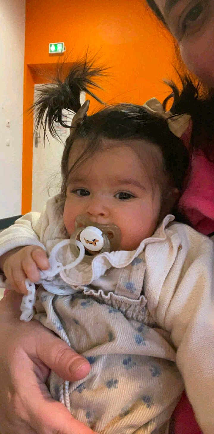 Ayla participe au concours pour gagner de l'argent avec cette photo : baby, child, pacifier, pigtails, person, indoor, orange_wall, adult_hand, clothing, cute, holding, portrait, infant, face, expression, closeup, warm_colors, hair_bows, casual, comfort