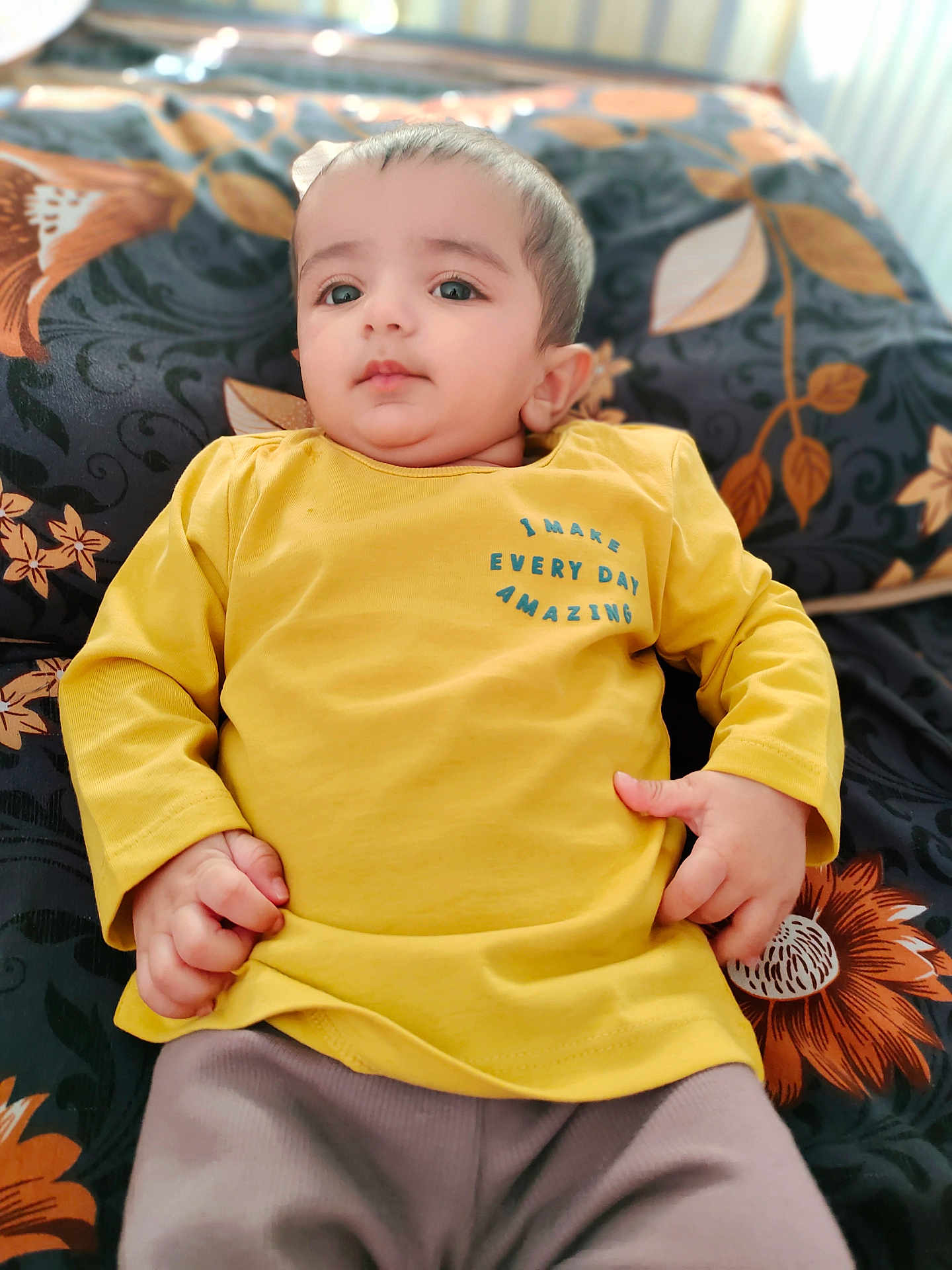 Shahzain joined the competition — help win amazing prizes! baby, child, yellow_shirt, lying_down, blanket, floral_pattern, curious_expression, indoors, portrait, young_child, clothing, hand, face, head, person, soft_lighting, casual_wear, cute, small_hands, comfortable