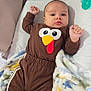 baby, infant, child, brown_outfit, turkey_design, blanket, dinosaur_print, bed, soft_fabrics, pacifier, cute, lying_down, indoors, sleepwear, raised_fists, portrait, young_child, cozy, comfort, awake