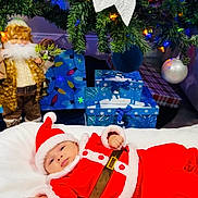 Nathan is registered to the contest to win money with this photo: baby, beard, blue_ornaments, celebration, christmas_lights, christmas_tree, decorations, doll, festive, festivity, gift_boxes, holiday, holiday_spirit, indoor, ornaments, red_clothing, santa_claus_outfit, toddler, white_blanket, winter