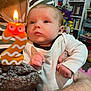 Briar is registered to the contest to win money with this photo: baby, birthday_candle, cupcake, chocolate, hand, tattoo, striped_shirt, bookshelf, toys, indoor, person, face, celebration, candle_flame, white_clothing, closeup, child, adult, holding, curious