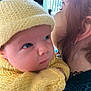 Briar is registered to the contest to win money with this photo: baby, infant, knit_hat, knit_sweater, yellow_clothing, person, curly_hair, indoor, closeup, face, portrait, holding, adult, child, warm_lighting, cozy, soft_focus, curious_expression, headwear, eyelashes