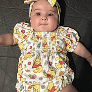 Ellie is registered to the contest to win money with this photo: baby, infant, child, winnie_the_pooh, headband, clothing, cute, smiling, lying_down, patterned_outfit, face, skin, eyes, mouth, arm, hand, fabric, flower_pattern, red, yellow