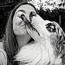 woman, dog, outdoor, black_and_white, face, smiling, licking, affection, close_up, nature, trees, pet, fur, long_hair, happy, friendship, portrait, animal, canine, love