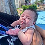 Hazel joined the competition — help win amazing prizes! baby, child, infant, person, face, tongue_out, curly_hair, mittens, outdoor, daylight, holding, arm, shirt, building, sky, clouds, tree, pool, greenery, hand