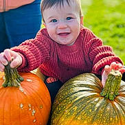 Elliott is registered to the contest to win money with this photo: baby, child, pumpkin, autumn, outdoor, grass, smiling, sweater, red_clothing, person, nature, seasonal, fall, harvest, cute, happy, face, holding, green, orange