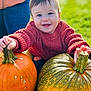 baby, child, pumpkin, autumn, outdoor, grass, smiling, sweater, red_clothing, person, nature, seasonal, fall, harvest, cute, happy, face, holding, green, orange