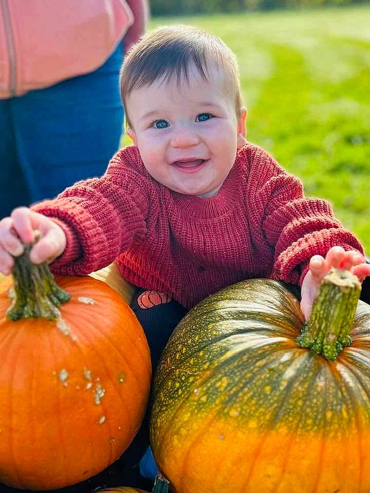 Elliott is registered to the contest to win money with this photo: baby, child, pumpkin, autumn, outdoor, grass, smiling, sweater, red_clothing, person, nature, seasonal, fall, harvest, cute, happy, face, holding, green, orange