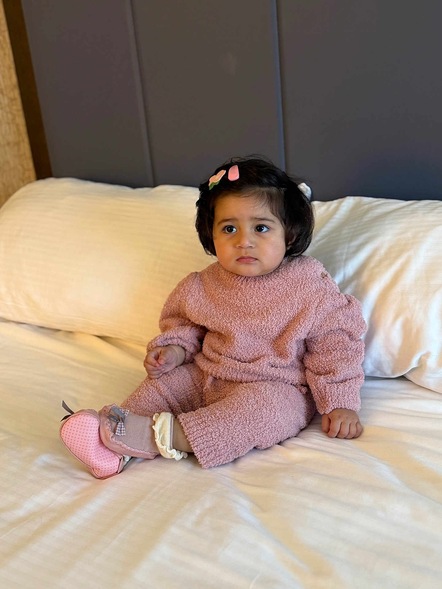 Aayat joined the competition — help win amazing prizes! toddler, child, pink_outfit, bed, white_bedspread, hair_clip, pink_shoes, indoors, portrait, cute, cozy_clothing, sitting, young_child, person, soft_lighting, neutral_background, expression, baby, candid, comfortable