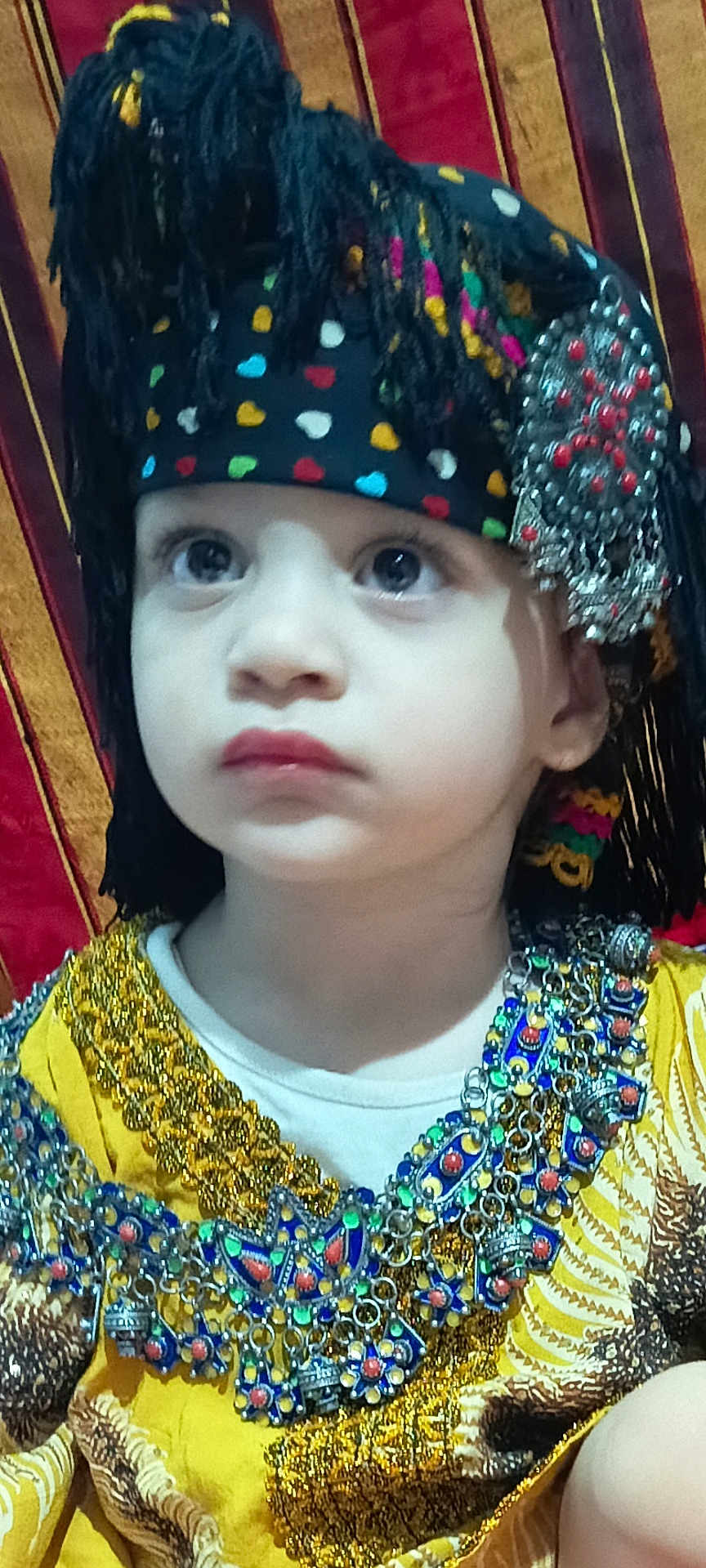 Tindaya a rejoint le concours — aidez-le/la à gagner de superbes lots ! child, face, headwear, jewelry, traditional_clothing, colorful, portrait, young, expression, beads, tassels, fabric, closeup, costume, cultural, decorative, patterned, indoors, serious, accessory
