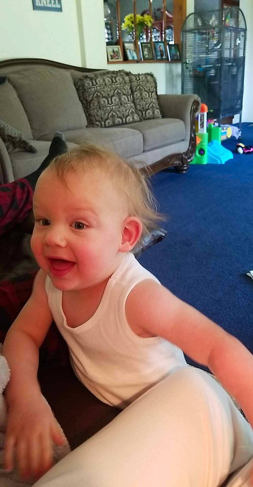 Tyler is registered to the contest to win money with this photo: baby, baby_toddler_clothing, blond, cheek, chest, child, comfort, couch, flooring, foot, hair, happy, human_leg, knee, person, sitting, smile, t_shirt, thigh, toddler