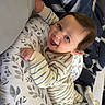 baby, bed, blanket, child, cozy, cute, face, floral_pattern, happy, indoors, infant, lying_down, person, pillow, playful, resting, sleepwear, smiling, striped_pajamas, young_child
