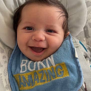 Roman is registered to the contest to win money with this photo: baby, infant, smile, happy, mohawk, bib, clothing, baby_seat, straps, face, child, cute, indoors, pattern, expression, person, young, cheerful, joyful, closeup