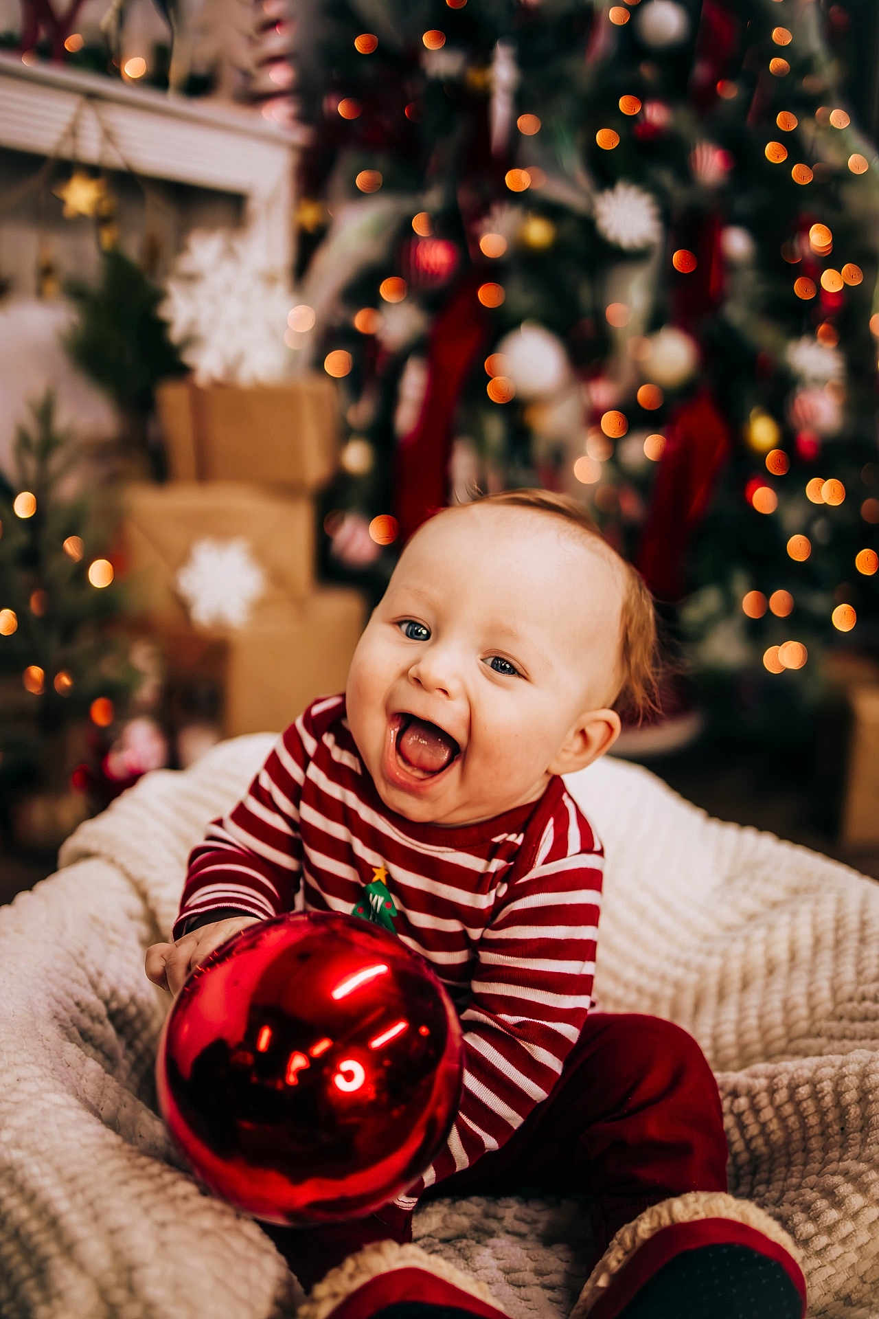 Kyland is registered to the contest to win money with this photo: baby, child, christmas, holiday, ornament, red, striped_clothing, smiling, happy, indoors, decorations, tree, lights, blanket, festive, cute, cozy, celebration, toddler, joy