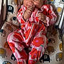 baby, infant, smiling, onesie, floral_pattern, elephant_pattern, cushioned_seat, hand, carpet, cute, happy, child, indoors, portrait, footwear, zipped_onesie, colorful_clothing, person, baby_garment, seated