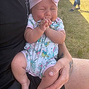 Maeve joined the competition — help win amazing prizes! baby, infant, child, person, arm, hand, tattoo, clothing, onesie, bow, headwear, outdoor, grass, sunlight, smile, closed_eyes, legs, feet, human, casual