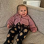 baby, child, couch, cozy, cute, face, footed_pants, furniture, happy, home, indoor, infant, knitwear, pants, person, relaxed, remote_control, seated, smile, sweater