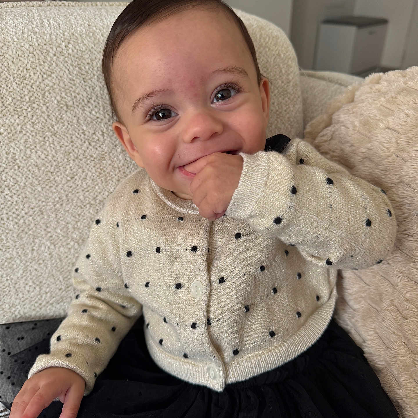 Ambre a rejoint le concours — aidez-le/la à gagner de superbes lots ! baby, child, smiling, sweater, black_skirt, couch, cushion, indoor, happy, cute, portrait, hand, face, person, young_child, cozy, clothing, seated, home, furniture