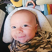 Jaxson joined the competition — help win amazing prizes! baby, smiling, face, infant, cushion, clothing, camouflage, toy, soft_toy, blue_eyes, head, person, happy, indoor, closeup, child, cute, baby_girl_or_boy, infant_garment, resting