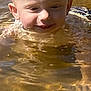 child, toddler, water, outdoor, blond_hair, wet_hair, smile, face, sunlight, reflection, nature, play, summer, happy, head, person, water_surface, ripples, skin, closeup