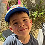 child, boy, smile, cap, hat, outdoor, sunlight, wall, greenery, shirt, dinosaur, jurassic_world, happy, portrait, casual_clothing, daylight, young, cute, playful, nature