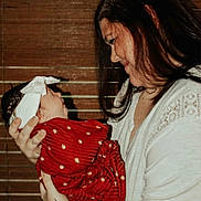 Gracelynn is registered to the contest to win money with this photo: woman, baby, holding, smile, red_blanket, headband, tattoo, indoor, portrait, face, person, closeup, warm_lighting, wooden_blinds, white_shirt, love, family, care, affection, mother