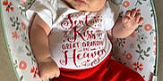 Gracelynn is registered to the contest to win money with this photo: baby, infant, curly_hair, red_pants, white_shirt, floral_pattern, cushion, bare_feet, infant_clothing, lying_down, indoor, cute, child, portrait, small_hands, small_feet, expression, comfort, soft_fabric, casual