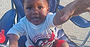 Jeremiah joined the competition — help win amazing prizes! child, toddler, boy, chair, outdoor, summer, clothing, shirt, shorts, footwear, flip_flops, hand, face, expression, sunlight, pavement, parking_lot, toy, sippy_cup, determined