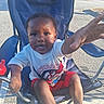 child, toddler, boy, chair, outdoor, summer, clothing, shirt, shorts, footwear, flip_flops, hand, face, expression, sunlight, pavement, parking_lot, toy, sippy_cup, determined